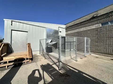 Galvanized chain link enclosure around mechanical equipment beside a building