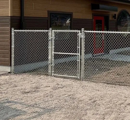 Galvanized pedestrian gate in a commercial chain link fence beside a building