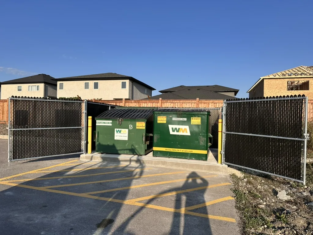 Chain link garbage enclosure with black privacy inserts and open double gates around two dumpsters