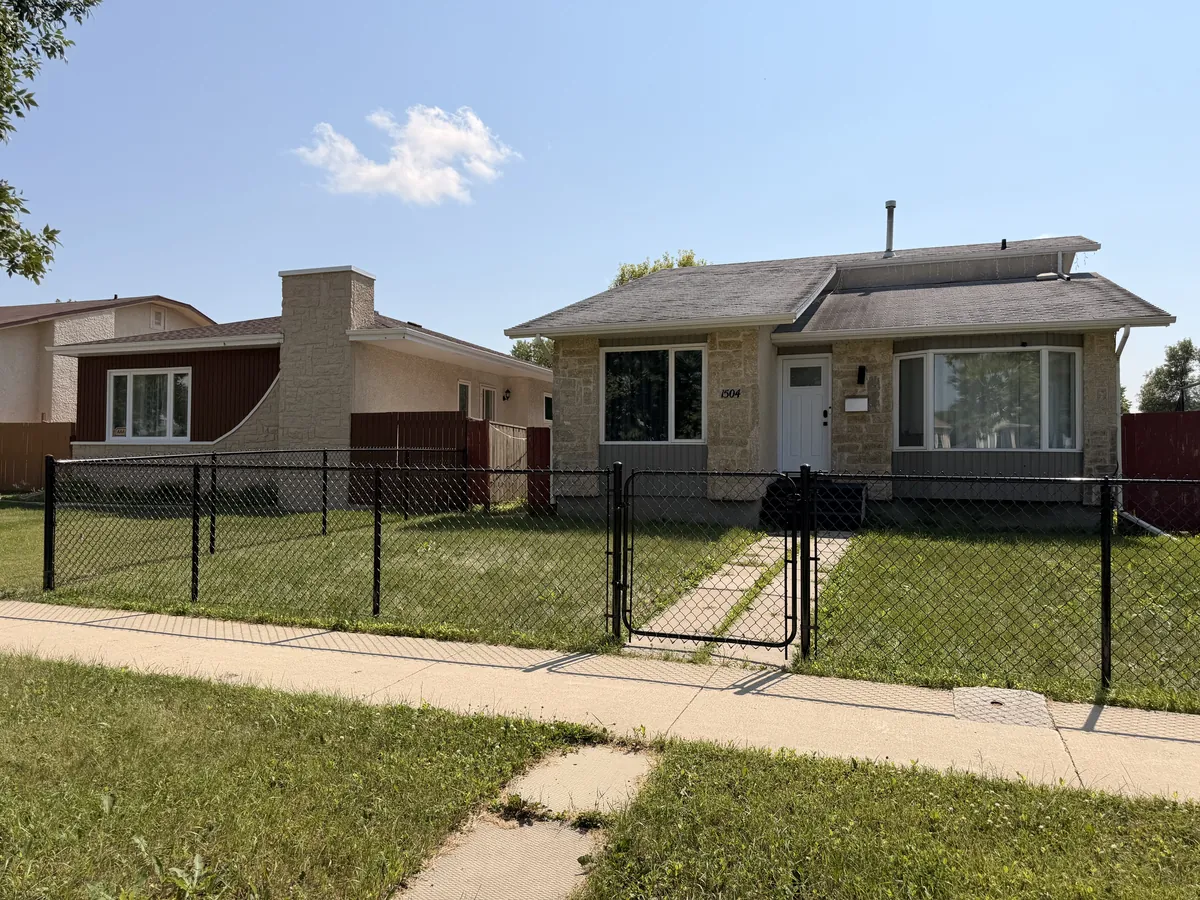 Black chain link fence and walk gate across the front yard of a bungalow