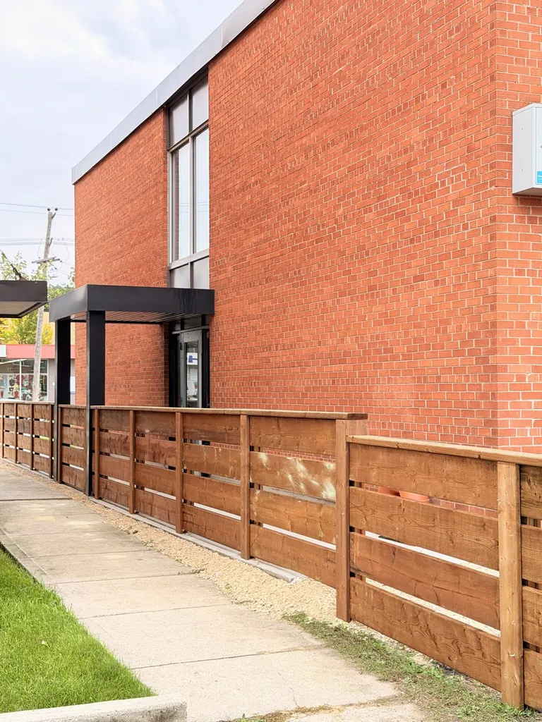 Long horizontal cedar fence on steel posts along a building walkway
