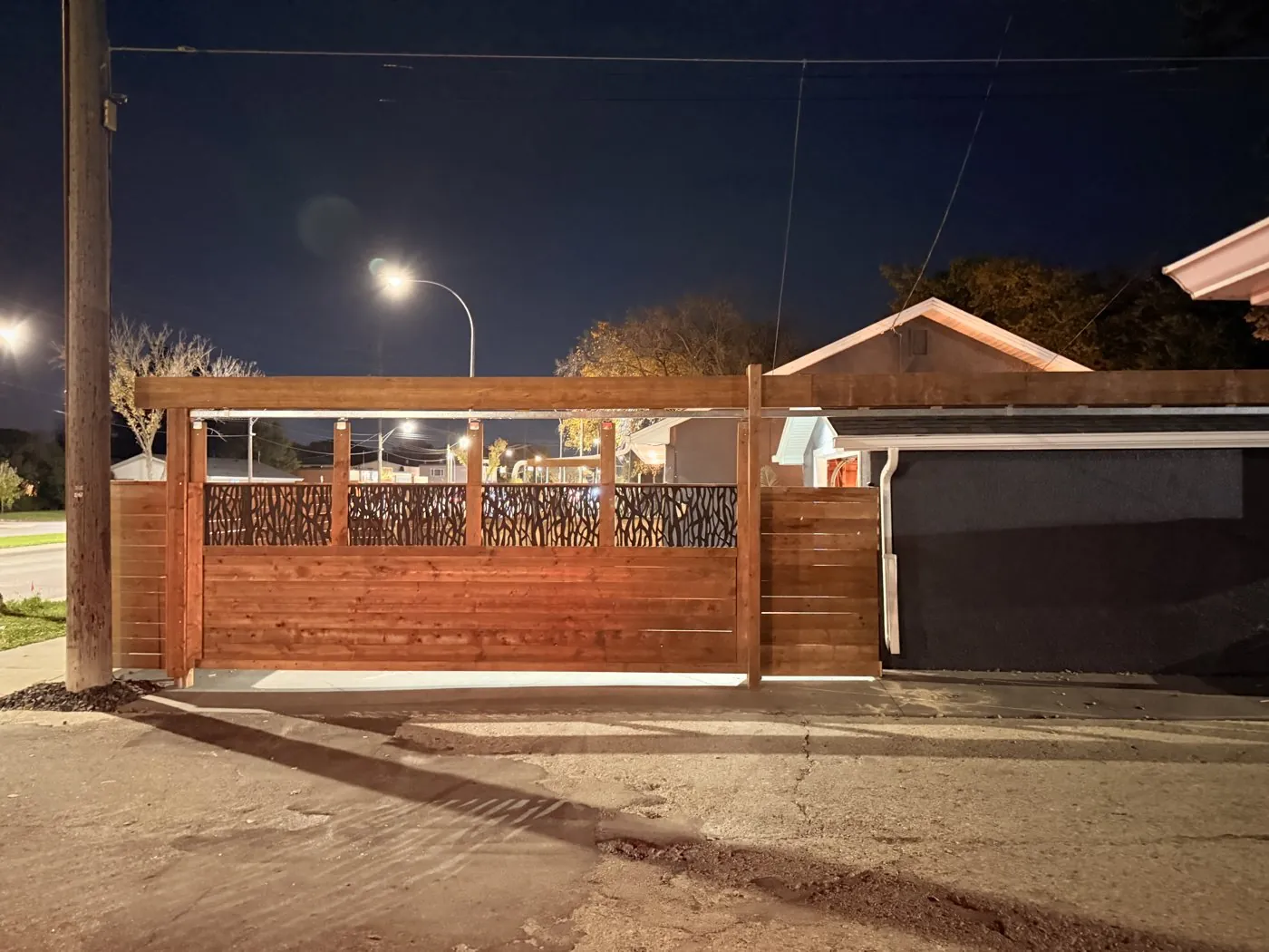 Horizontal wood fence and slide gate with decorative metal panels at night