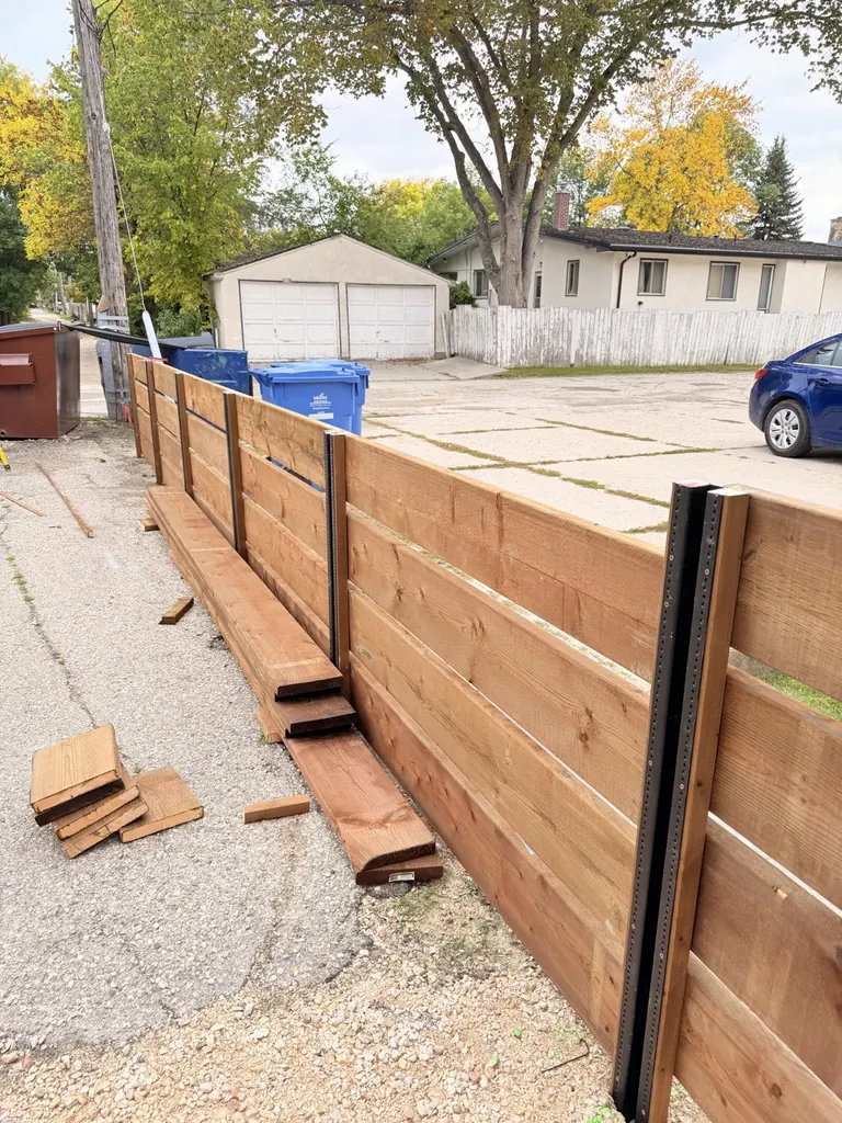 Black PostMaster steel post with its flange of screw points, with cedar boards going on